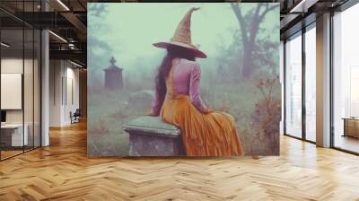 Vintage film still of a witch in a pink and mustard velvet dress and hat, sitting on a tombstone in a foggy graveyard. Wall mural