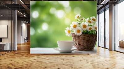  A cup of tea and a small basket with daisies on the table against a green spring background.  Wall mural