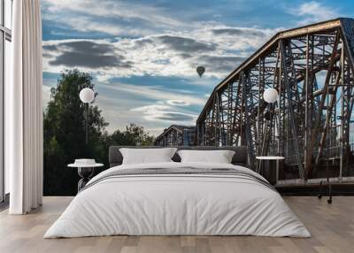 a flying hot air balloon over a bridge in a summer evening on a cloudy day Wall mural