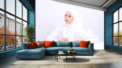 Portrait of a beautiful girl indonesia wearing elegant hijab, looking up, front view, hands holding cosmetic cream on a white table for daily facial care routine needs a white background. Perfect skin Wall mural