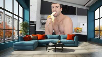 Shirtless man eating a banana in the kitchen  Wall mural