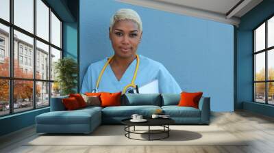 Young serious afro american nurse standing at hospital ward with clipboard and pen in hand. Neutral expression, looking at camera. Wall mural