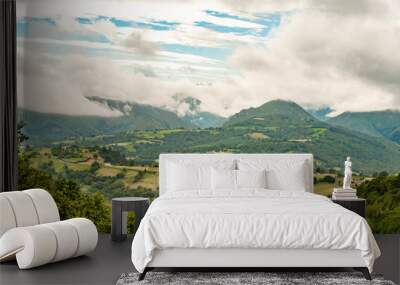 A panoramic view of white peaks mountains covered with dramatic clouds alternating with fresh green lawns Wall mural