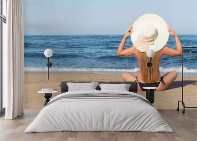 Young woman sitting on a sea beach with hat. Summer vacation Wall mural