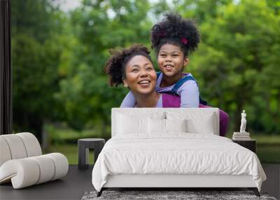 African American mother is playing piggyback riding with her young daughter while having a summer picnic in the public park for wellbeing and happiness concept Wall mural