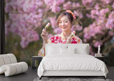 Japanese woman in traditional kimono dress holding sweet hanami dango dessert while walking in the park at cherry blossom tree during spring sakura festival with copy space Wall mural