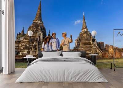 Thai local tour guide is explaining the history of old Siam to the couple of tourist on their backpacker honeymoon travel to ancient temple of Ayutthaya, Thailand Wall mural