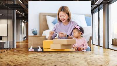 Young Asian mother is packing the merchandise product package while working at home ready to deliver while her toddler kid is playing around with her toy Wall mural