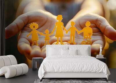 A pair of hands holding yellow paper cutouts representing people, including one person in an empty wheelchair and another with the arms crossed to represent parents or family members Wall mural