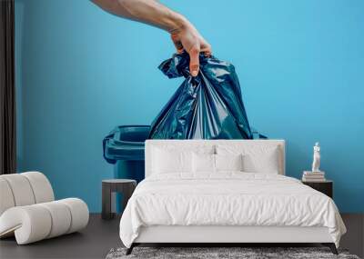 Close up of hand putting a black garbage bag into a trash bin isolated on a blue background, in a closeup view  Wall mural