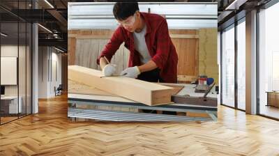 young man Asian carpenter with red shirt  in workshop store working on wood plank and measurement tools work from home Wall mural