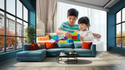 Asian cute brother and sister play with a toy block designer on the table in living room at home. Concept of bonding of sibling, friendship and learn through play activity for kid development. Wall mural