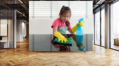 Asian Cute preschool student girl washing glass table with green towel in living room at home, with water and detergent solution spray. Wall mural