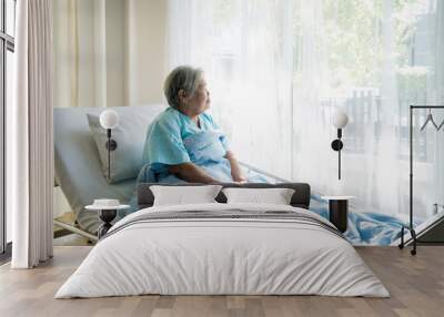 Asian depressed elderly woman patients lying on bed looking out the window in hospital. Elderly woman patients is glad recovered from the illness. Wall mural