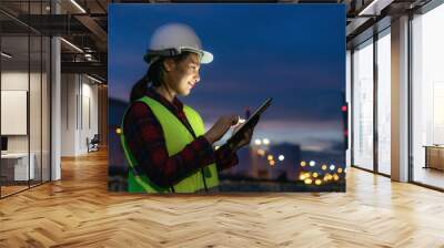 Asian woman petrochemical engineer working at night with digital tablet Inside oil and gas refinery plant industry factory at night for inspector safety quality control.. Wall mural