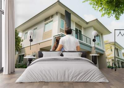 Back portrait of Asian young couple standing and hugging together looking happy in front of their new house to start new life. Family, age, home, real estate and people concept.. Wall mural