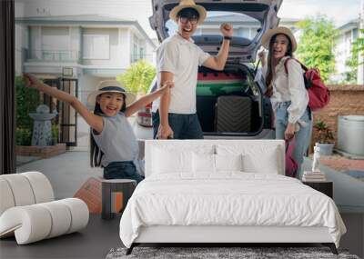 Portrait of Asian family with father, mother and daughter looks happy while preparing suitcase into a car for holiday. Shot in the house garage.. Wall mural