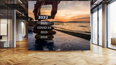 Happy new year 2022 is coming concept. Man adding stone to pebble tower because new year 2022 replace 2021. Beautiful conceptual photo with text for holiday and greeting cards. Wall mural