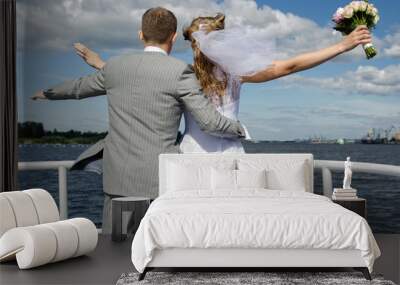 Bride and groom standing in front of the yacht in the wind. Wall mural