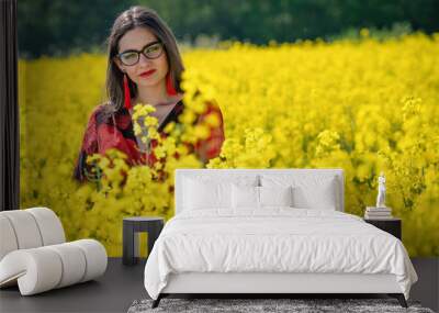 Young woman with glasses standing in yellow oilseed rape field image Wall mural