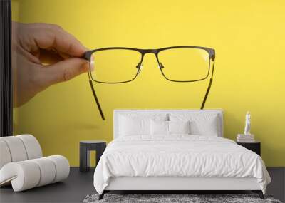 Hand holding plastic black glasses, isolated on yellow background. Wall mural