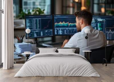 Businessman working at desk analyzing financial data on three computer screens in modern office, finance concept Wall mural