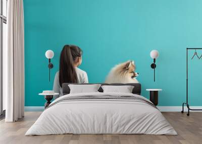 Cute Pomeranian dog sitting beside a young boy with his back turned, both against a teal background, creating an adorable and innocent scene with copy space. Concept: childhood companionship, pet frie Wall mural