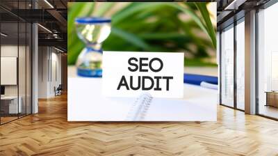 Seo audit - business concept text on a white notebook and hourglass, blue pen, green flowers Wall mural