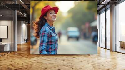 One young European woman smiling, wearing a red hat and plaid shirt, standing on a city street, casual fashion, blurred street background with greenery, sunny day, joyful and cheerful mood, vertical f Wall mural