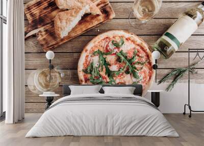 Italian pizza margherita with arugula, with a bottle and two glasses of white wine on a wooden table Wall mural