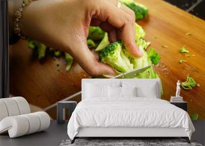 Close up of woman cutting broccoli with kitchen knife on cutting board while making lunch. Wall mural