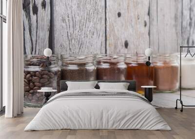 Coffee beans, coffee powder, creamer, cocoa powder, honey and processed tea leaves in a mason jar over weathered wooden background Wall mural