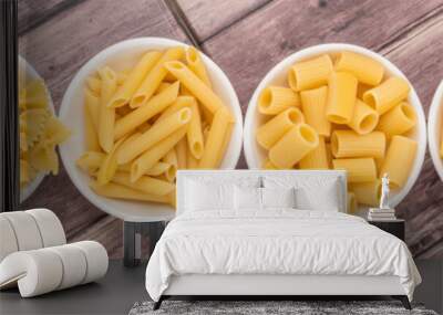 various dried pasta variety and shapes in white bowl over wooden background Wall mural