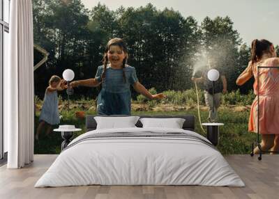 Dad and daughters play in the summer in the garden, a man sprinkles water on his daughters Wall mural