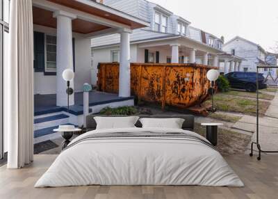 An old yellow scraped up dumpster in a driveway between two very close houses Wall mural