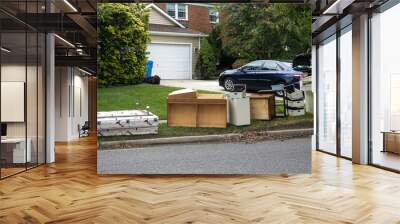 Discarded wooden furniture and an old bed lined up by the curb near a street waiting for trash pickup Wall mural