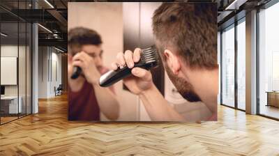 A man cuts his hair on his head with an electric razor  Wall mural