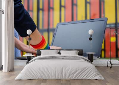 Close-up of woman hands with laptop and LGBT bracelet in modern park . LGBTQIA culture. Wall mural