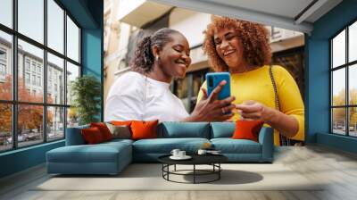 Gen z female friends using cellphone in the street. Close up view. African and latin ethnicities. Wall mural