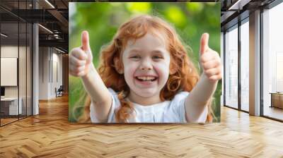 Joyful girl giving thumbs up, her face expressing happiness and delight, blurred greenery background. Wall mural