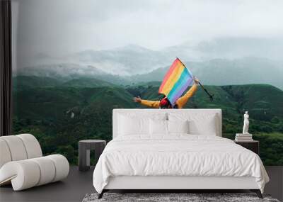 Hiker person on the mountain waving a rainbow gay pride flag. sport and inclusion. mountain activities- man with backpack doing trekking. Wall mural