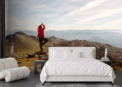 man on his back in red clothes and arms raised, practicing yoga with the tree pose and contemplating the mountain landscape after hiking up a mountain. sport, travel and adventure. meditation. Wall mural