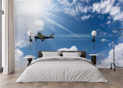 Small private propeller airplane in motion against a beautiful clear blue sky with cumulus clouds and sunbeams. Wall mural