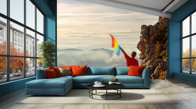 mountaineer man making summit on a mountain and waving a rainbow lgbt pride flag at sunset. lgbt movement and rights concept. Gay person climbing a mountain. sport and adventure Wall mural