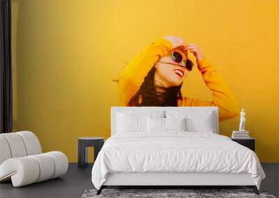 portrait of young Chinese woman in yellow sweater and sunglasses painted with lgbt pride rainbow flag posing with yellow background Wall mural