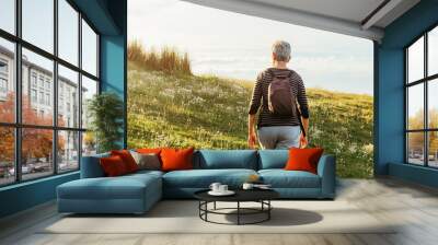 Retired woman with gray hair with backpack taking a walk in a natural setting at sunset. Old age and healthy lifestyle. Wall mural