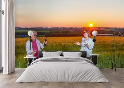 Man offers his wife some wine to celebrate the end of the day out in the field with the beautiful landscape that nature presents with the sunset. Wall mural