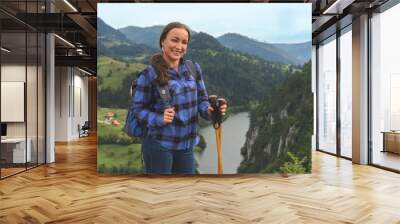 Young happy smiling woman in blue shirt, backpacker tourist, standing alone mountain ridge cliff edge, looking camera, portrait, scenic landscape view Wall mural