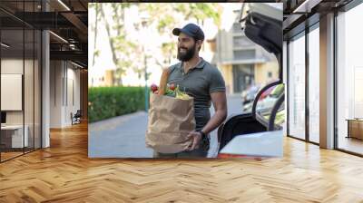 Young man with strong beard carrying  fresh groceries that he bought in super market. Wall mural