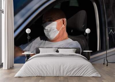 Senior man in medical mask driving a car, looking at the camera. coronavirus concept. respiratory protection Wall mural